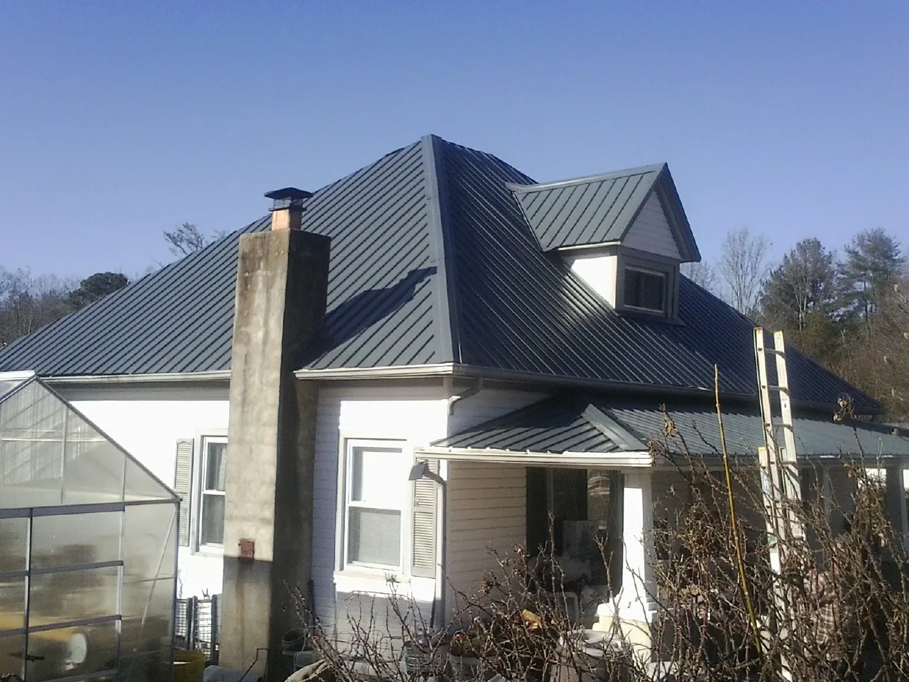 Dark blue standing seam metal roof on a white farmhouse with dormer — Slate & Tile Roof Repair by Roofing Brothers in Conesus