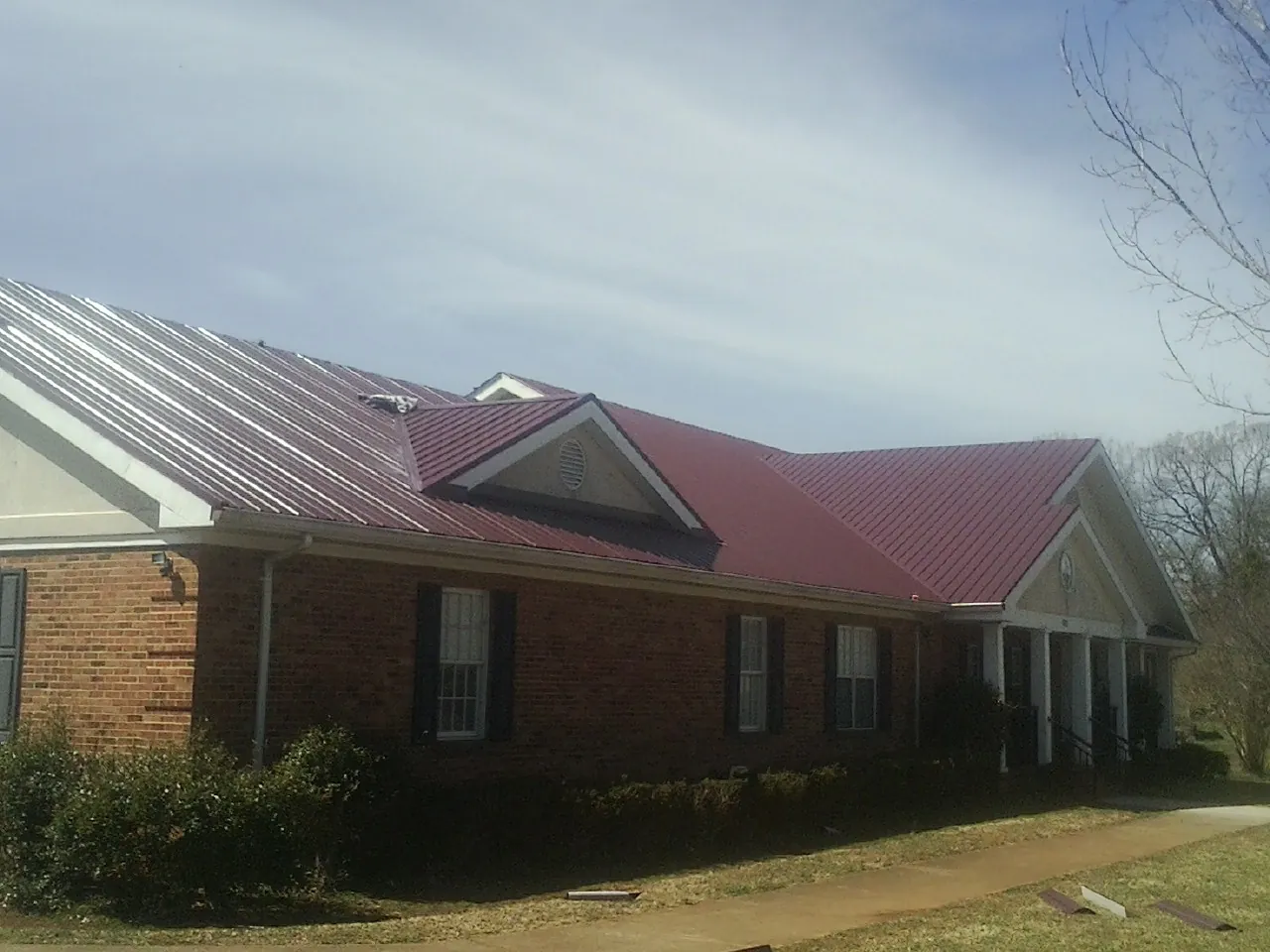 Red metal roof with gabled entries on a long brick building, from a Hail Damage Roof Repair job in Conesus