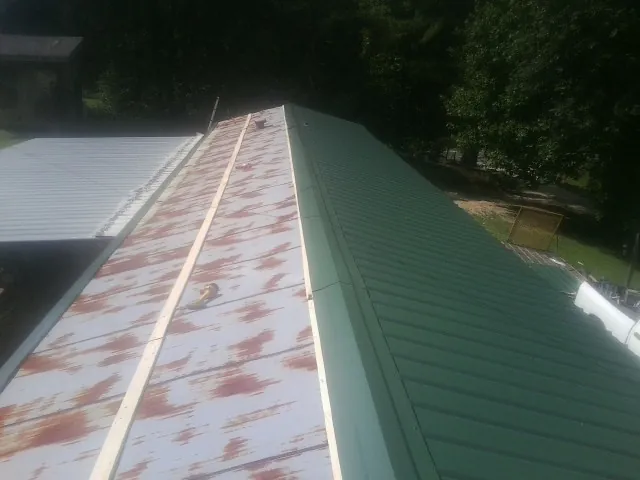 Old rusted panels beside newly installed green metal roofing — Wind Damage Roof Repair by Roofing Brothers in Conesus