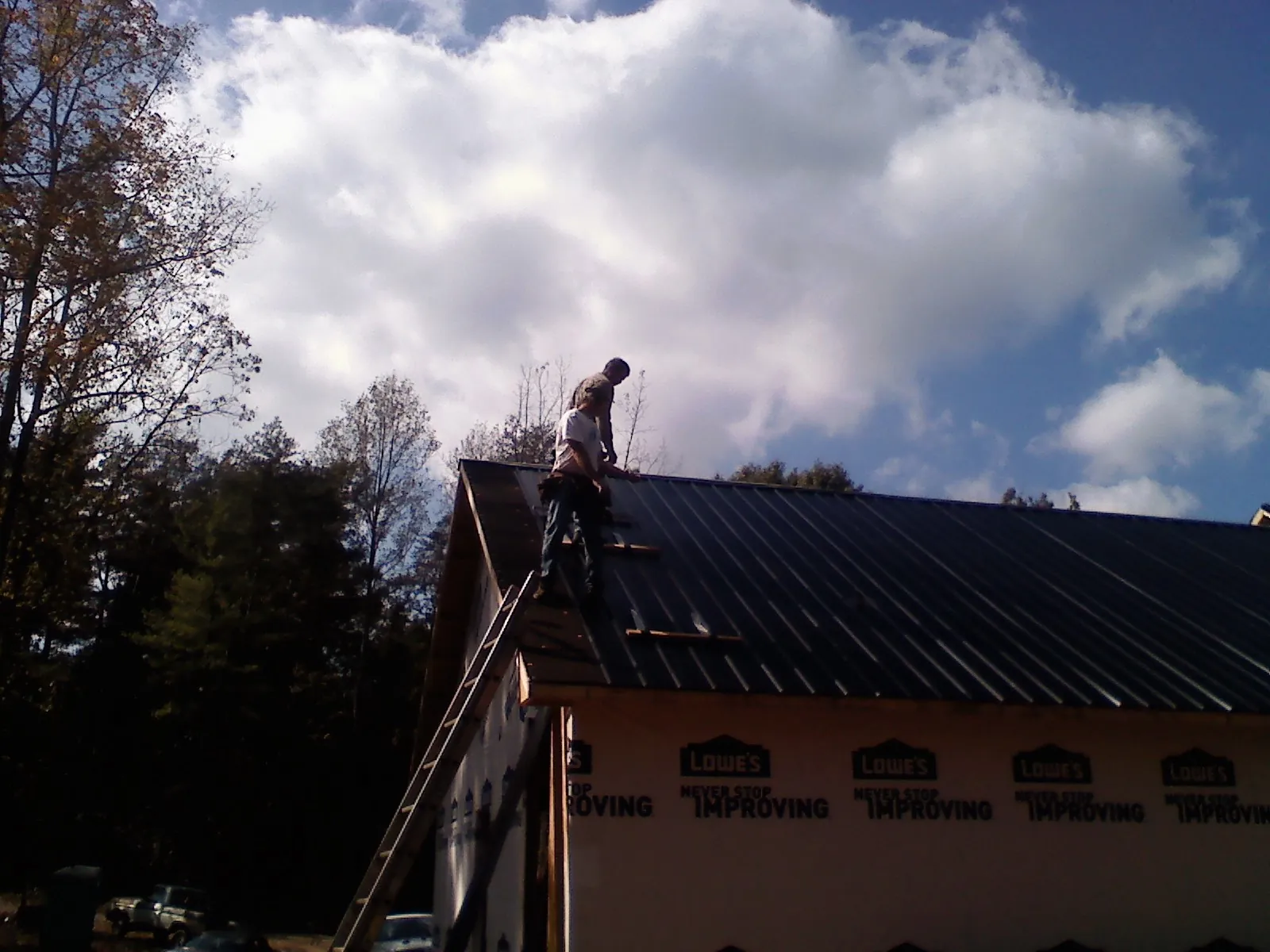 Roofer fastening dark metal panels high against a cloudy sky, from a Roof Inspection job in Conesus