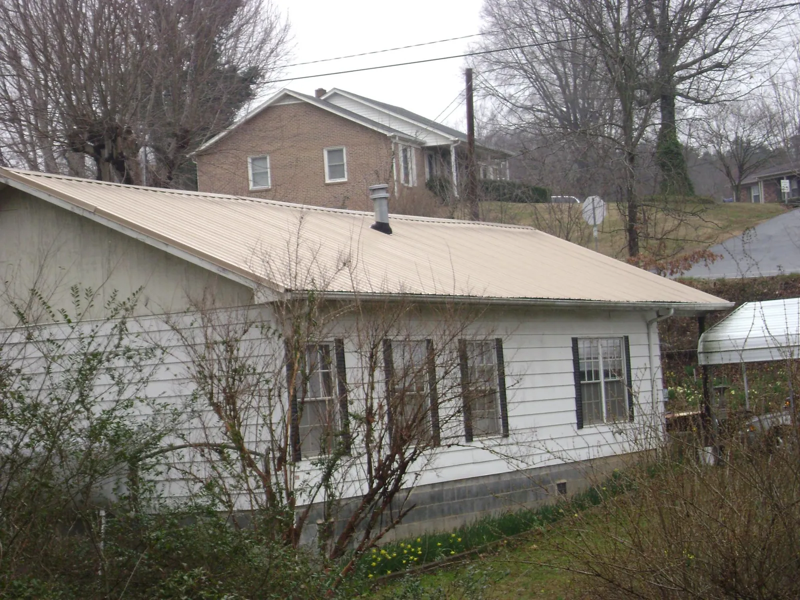 Tan metal roof on a white sided house set into a hillside — Commercial Roofing by Roofing Brothers in Conesus