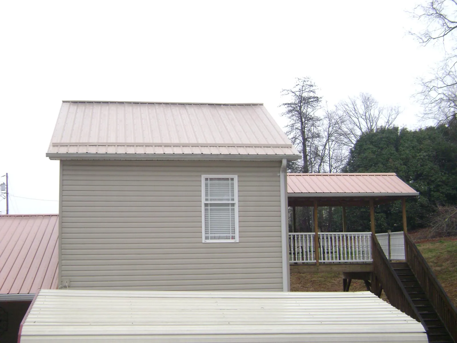 Tan metal roofs on a two story addition and attached porch, from a Roof Replacement job in Conesus